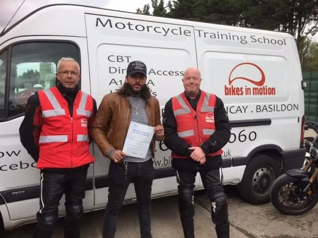 Pete Wicks holding his pass certificate, standing between two Bikes in Motion instructors in front of the school's van.