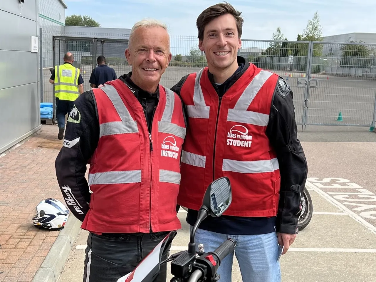 Alex Lynn smiling next to a Bikes in Motion instructor, both in red Bikes in Motion hi-vis vests.