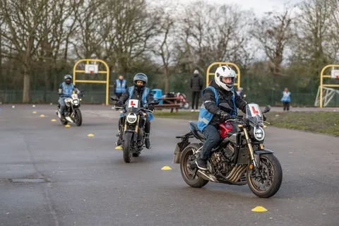 Three learners ride in a line along a cone lane, the nearest in a white helmet on a dark motorbike.