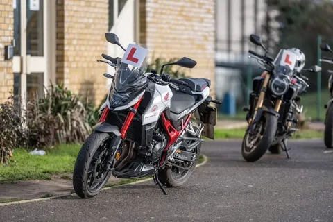 A white and red motorbike with an L plate parked beside a yellow-brick wall, with other bikes parked behind it.