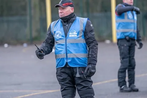 Two instructors in blue vests stand on the practice area in front of a basketball hoop, one of them gesturing.