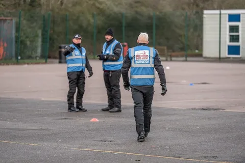 Three instructors in blue vests talk on the practice area, one of them walking towards the camera.