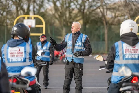 An instructor holds out a hand while explaining something to learners in blue student vests.