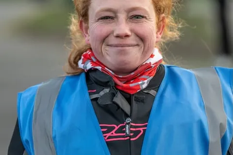 A smiling instructor with red hair wears a blue vest with the Bikes in Motion instructor logo.
