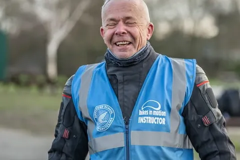 A laughing instructor with silver hair wears a blue Bikes in Motion instructor vest.