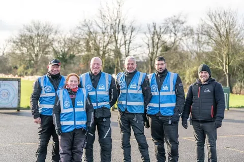 A group of instructors in blue vests pose together and smile on the training ground.