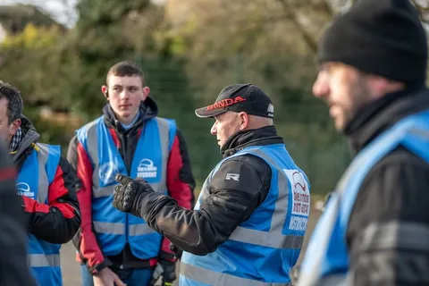 Learners and an instructor in a black cap stand close together in blue vests during a briefing.