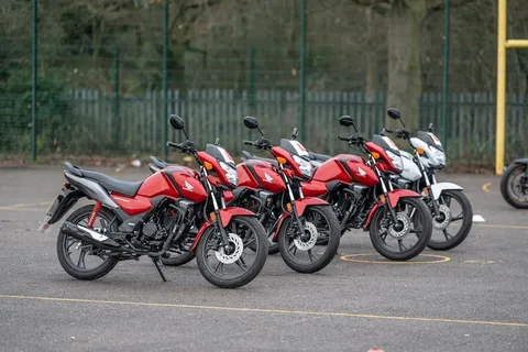A row of red learner motorbikes parked together on the practice area, with a white bike at the end.