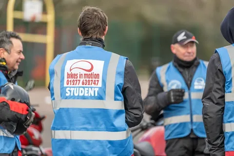 Learners and instructors stand together in blue vests, with a learner in a student vest in the foreground.