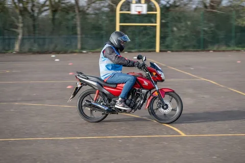 A learner in a black helmet rides a red motorbike across the practice area, leaning slightly into a turn.
