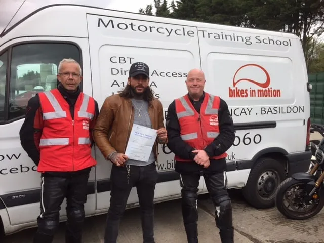 Pete Wicks holding his pass certificate, standing between two Bikes in Motion instructors in front of the school's van.